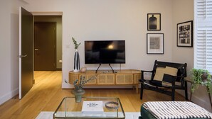 A modern living room with a flat-screen TV, a wooden bench, a glass coffee table, and a framed picture on the wall. - Brick Lane Duplex Styled Living (London)