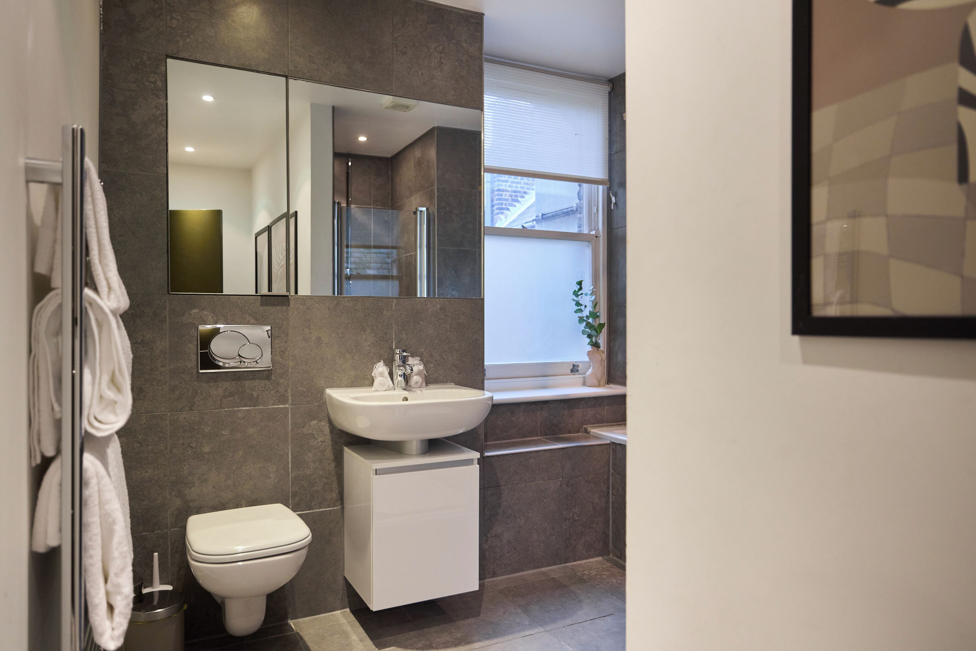 Une salle de bain moderne avec des toilettes blanches, un lavabo et un grand miroir.