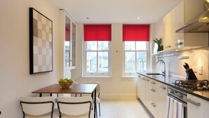 A modern kitchen with a dining table and chairs, a stove, and a window with red blinds. - Brick Lane Duplex Styled Living (London)