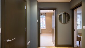 A hallway with a wooden floor, a round mirror on the wall, and a door leading to another room. - Brick Lane Duplex Styled Living (London)