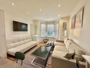 A modern living room with a sofa, a coffee table, and a TV mounted on the wall. - The Tube Station is Just a 10-minute Walk Away (London)