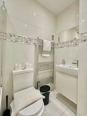A modern bathroom with a glass shower enclosure, a toilet, a sink, and a mirror. - The Tube Station is Just a 10-minute Walk Away (London)