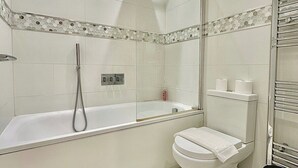 Un baño moderno con ducha envuelta en vidrio, un inodoro blanco y un cubo de basura negro.