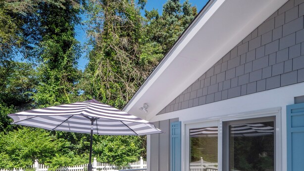 Un terrazzo con tavolo e sedie, un ombrellone a righe e un recinto di legno bianco.