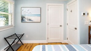 Una camera da letto con un letto, una porta, una finestra con persiane, un quadro appeso al muro e un porta scarpe.