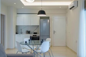 A modern kitchen with white cabinets, a glass dining table, and a black pendant light. - Irakleio Notos Boutique Apartments 1 (Iraklio)