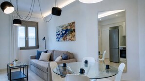 Una sala de estar moderna con una mesa de vidrio para comer, un sofá con cojines, una mesa de centro y un cuadro en la pared.