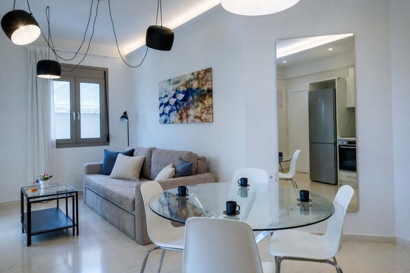 Una sala de estar moderna con una mesa de vidrio para comer, un sofá con cojines, una mesa de centro y un cuadro en la pared.