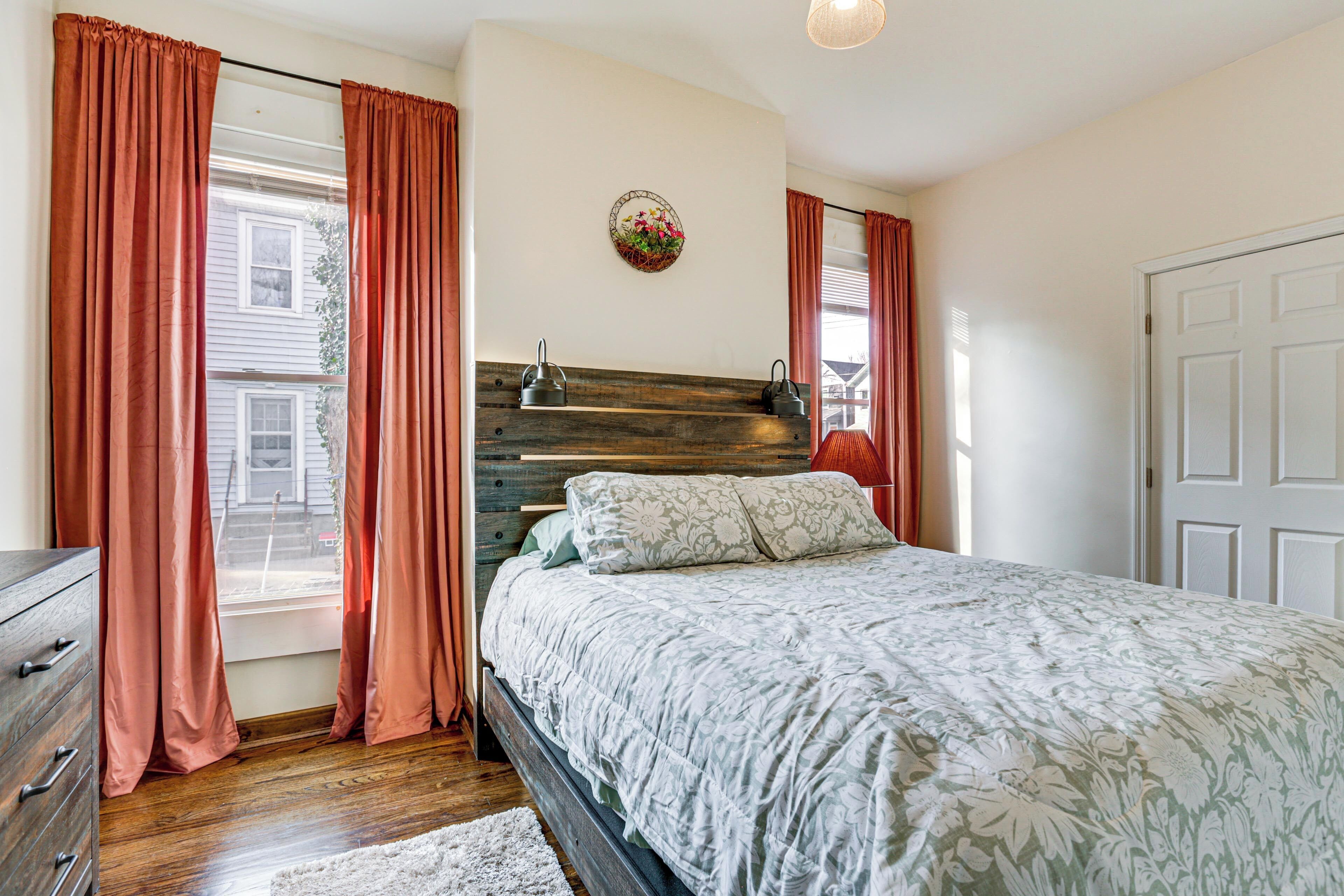 A bedroom with a wooden headboard, a bed with floral bedding, a dresser, and a window with curtains.