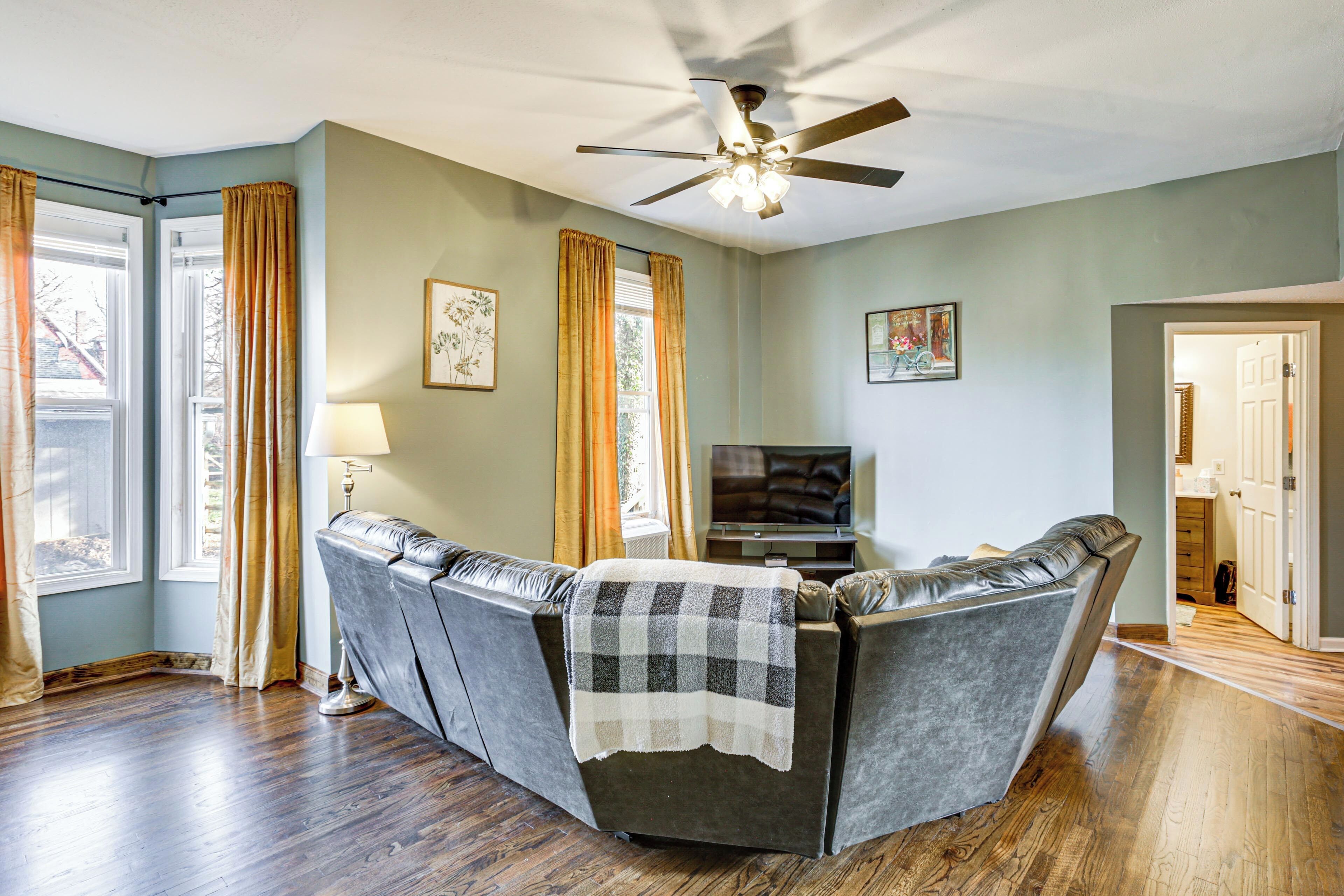 A living room with a sofa, a ceiling fan, and a television.