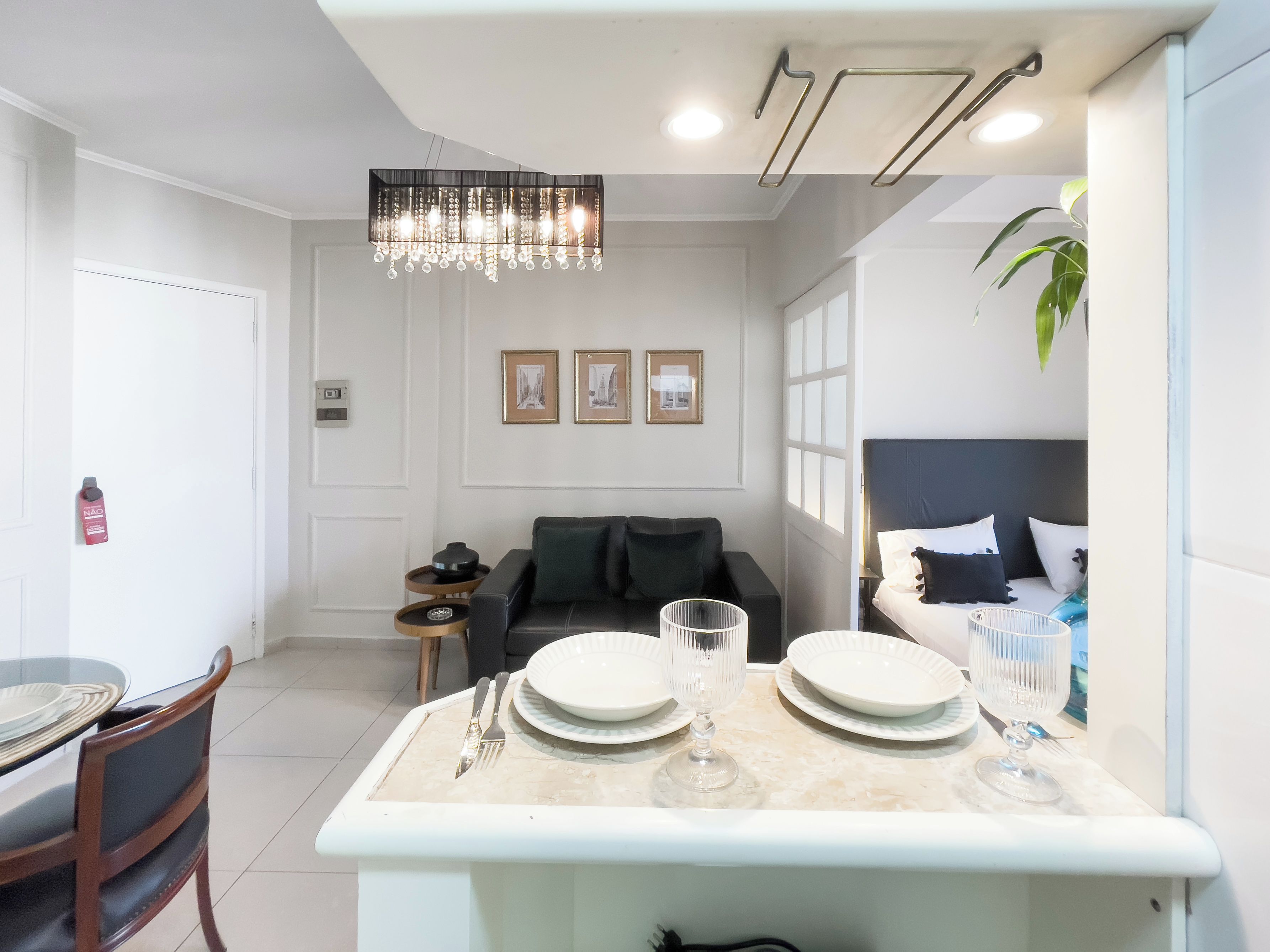 A modern living room with a dining area, featuring a chandelier, a sofa, a coffee table, and a bed with a headboard.