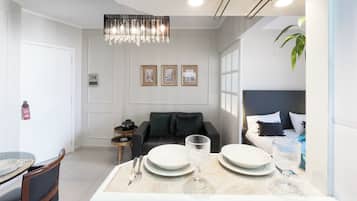 A modern living room with a dining area, featuring a chandelier, a sofa, a coffee table, and a bed with a headboard.
