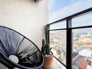Un balcón con una silla tejida negra y una planta en maceta.