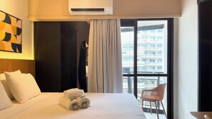 Een hotelkamer met een bed, een raam met uitzicht op gebouwen, een airconditioning en een stoel.