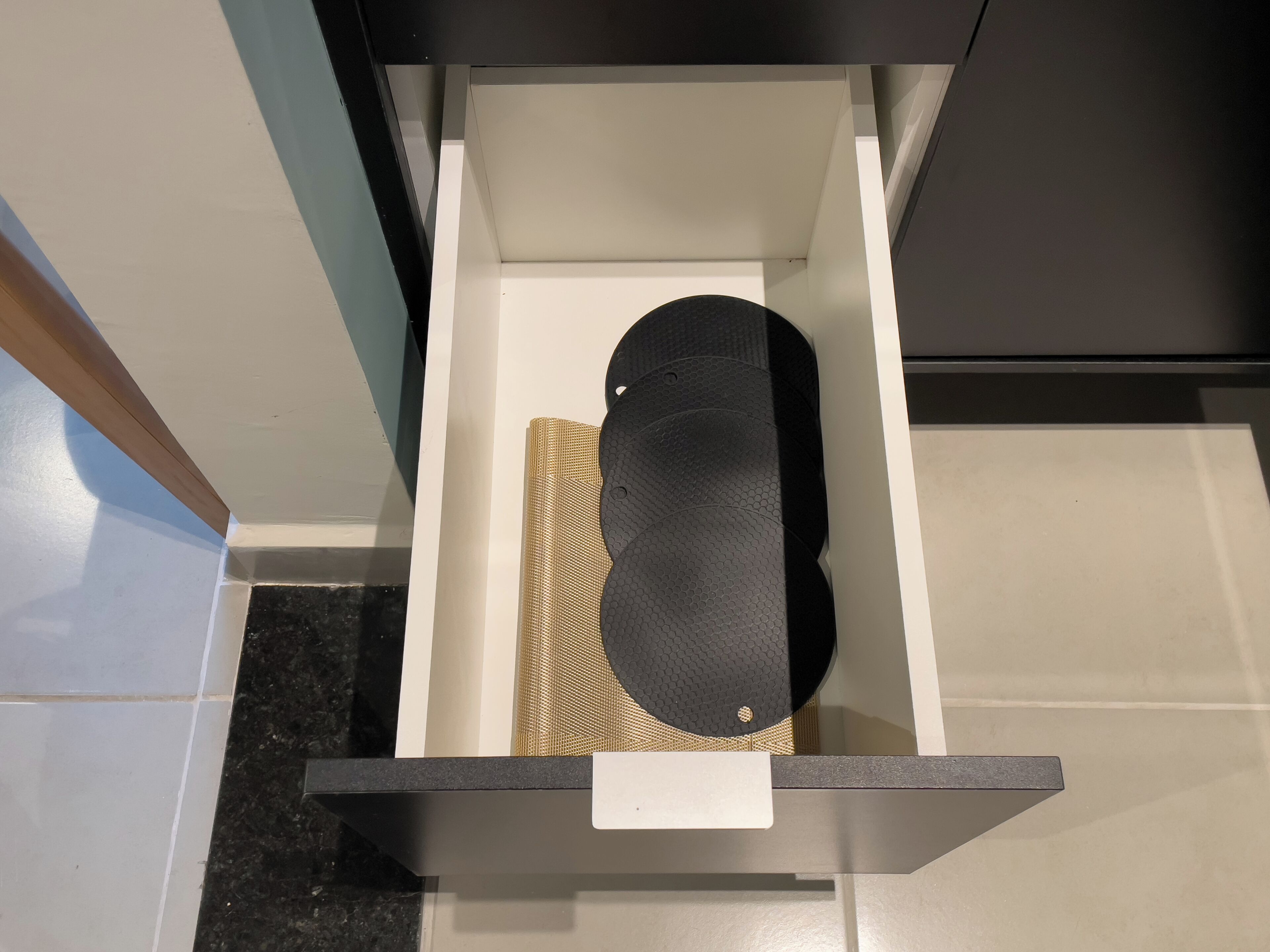 A kitchen drawer with a black object, possibly a kitchen tool, and a woven mat.