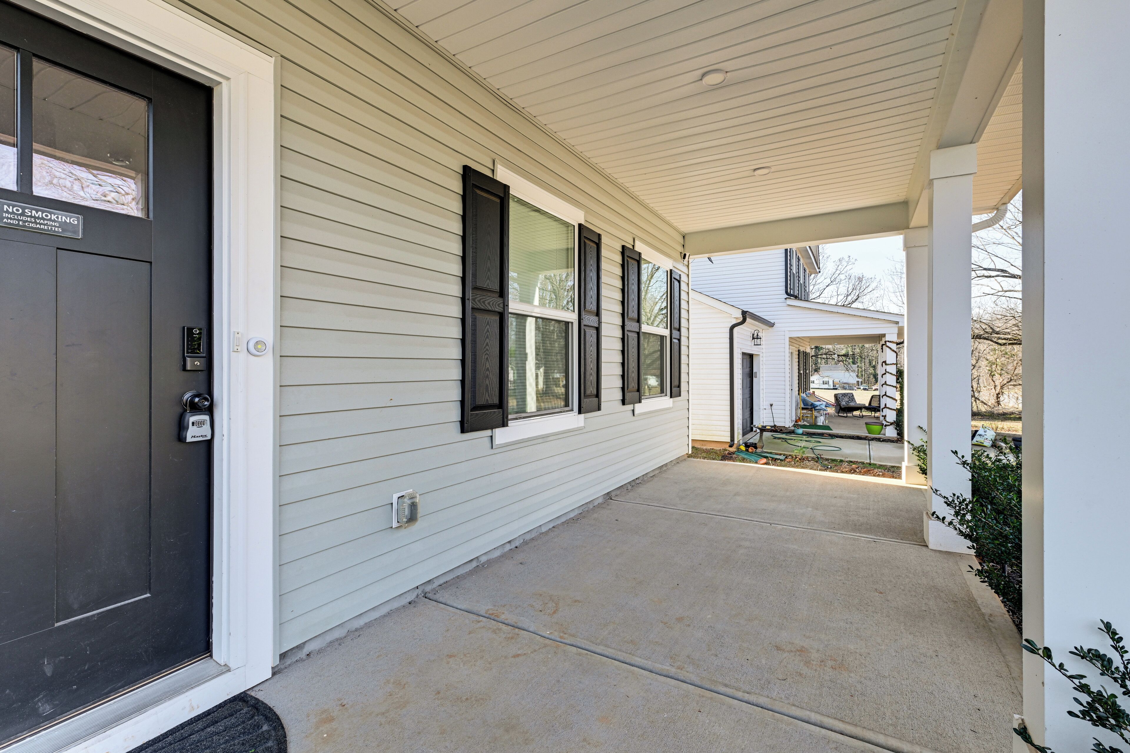 A covered porch with a black door, a sliding glass door, and a small garden area with a lawnmower and garden tools.
