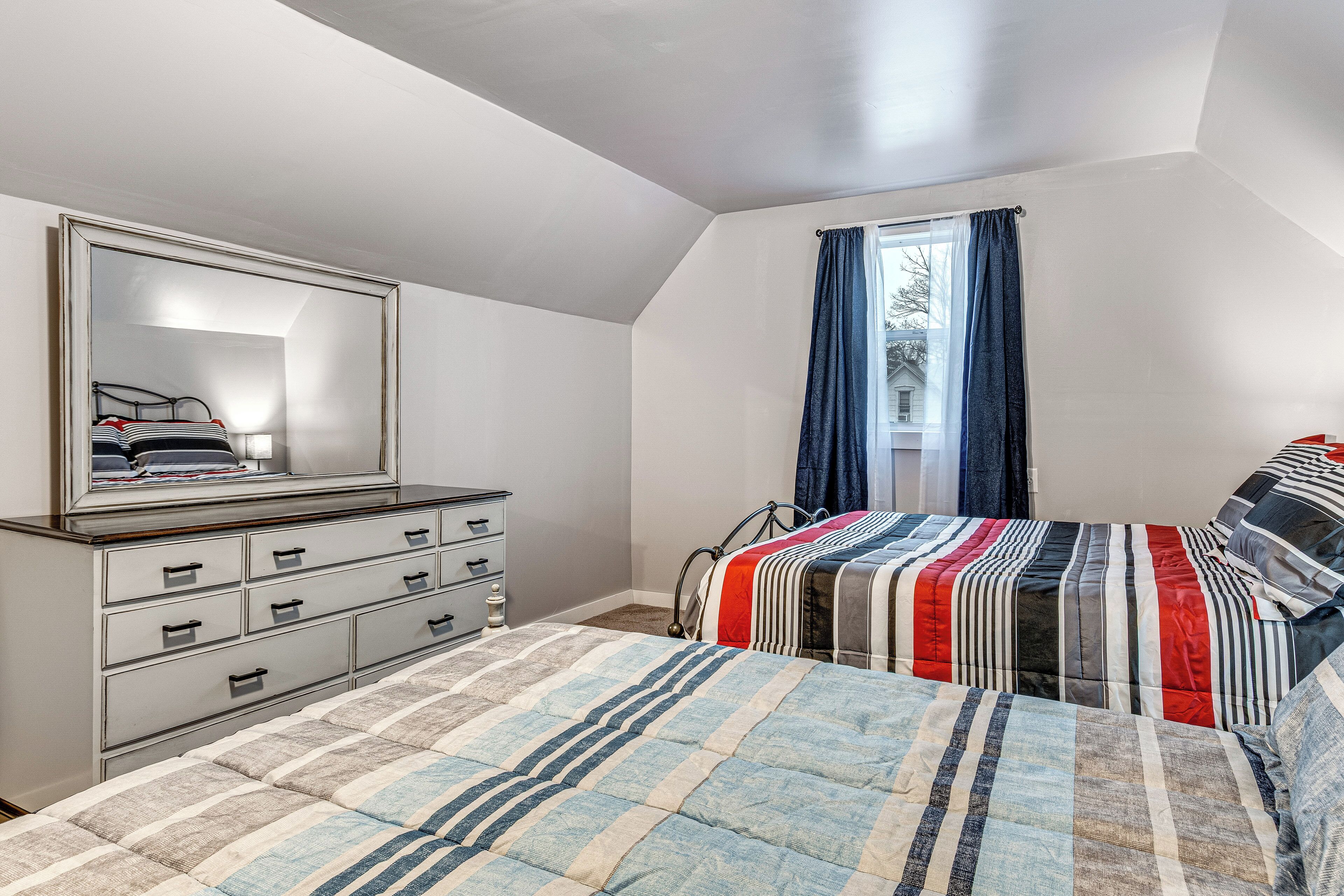 A bedroom with a bed, a dresser, a mirror, and a window with curtains.