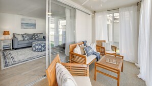 Una sala de estar moderna con un sofá, un reposapiés y sillas de madera. Hay una puerta de vidrio que da a un balcón.