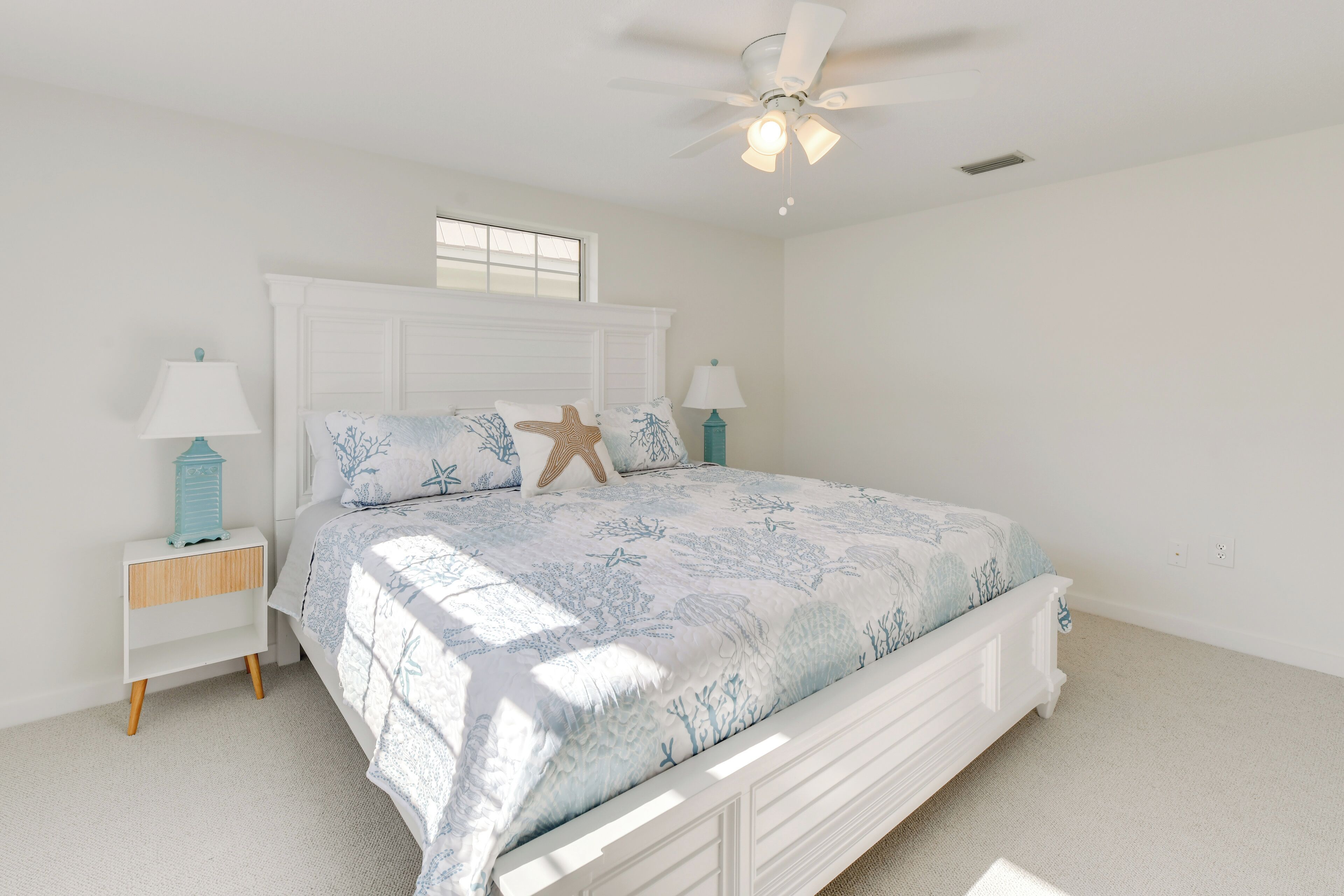 A bedroom with a bed, two bedside tables, a ceiling fan, and a window.