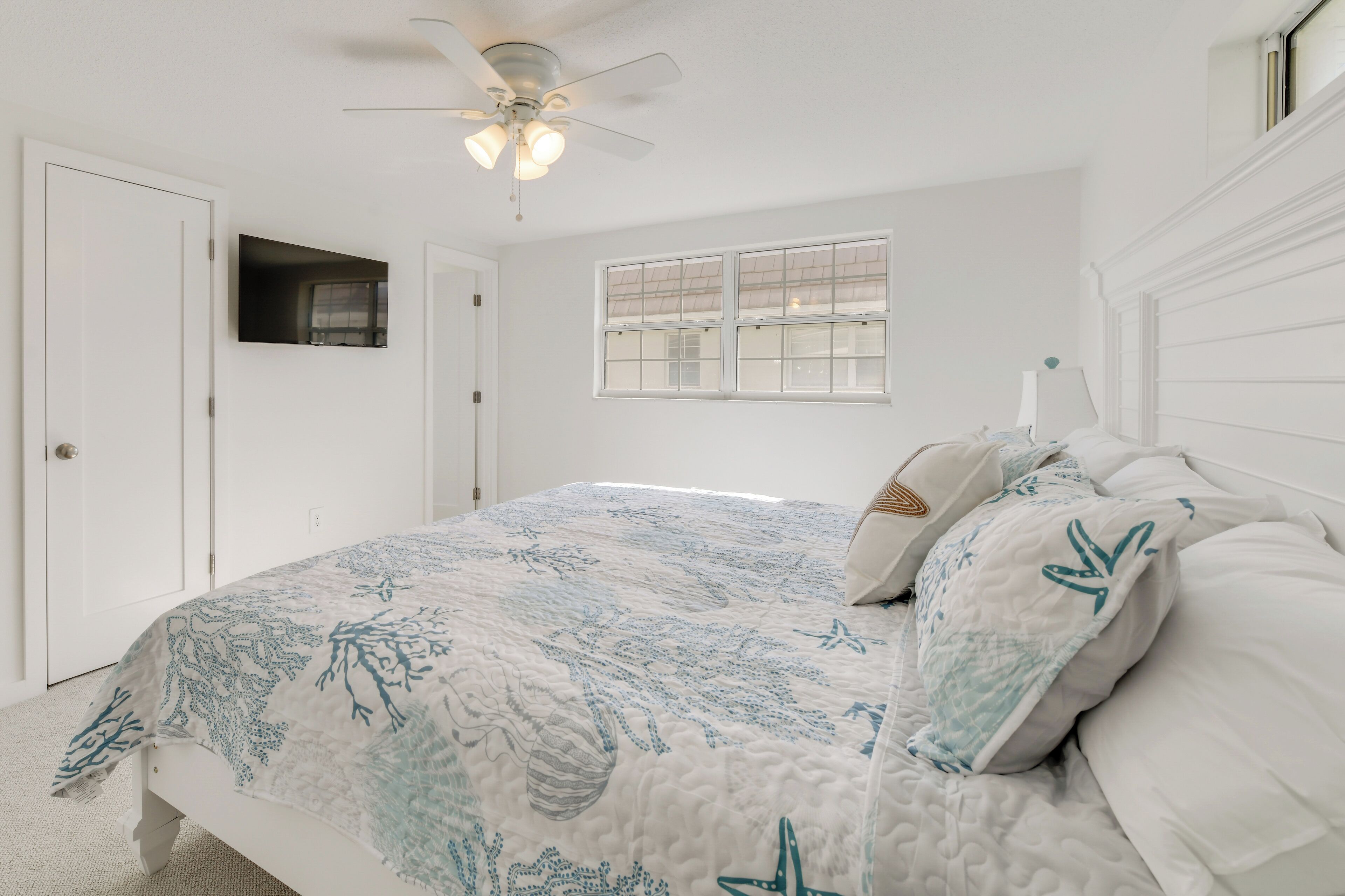 A bedroom with a bed, a ceiling fan, a window, and a door.