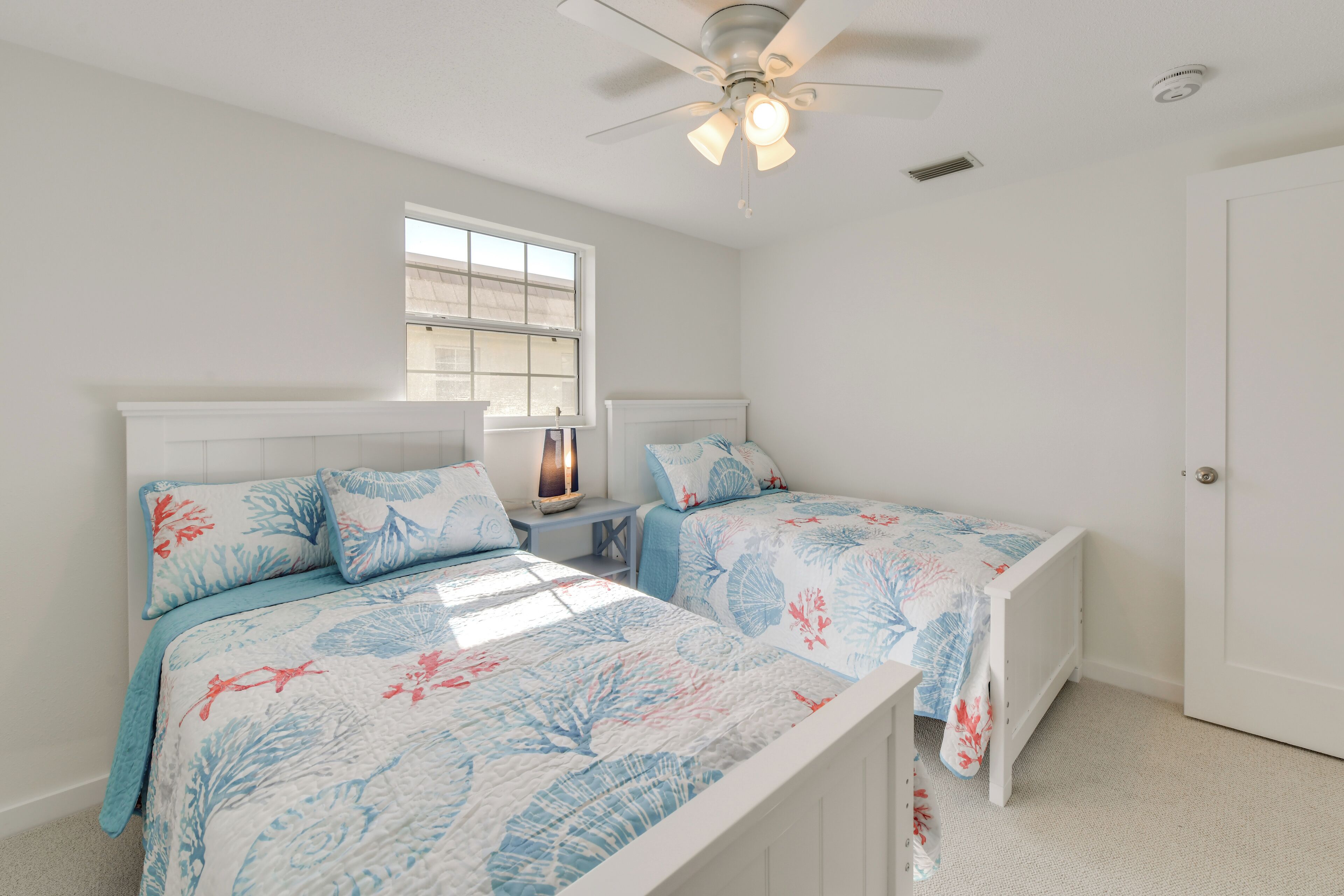 A bedroom with two beds, a window, a ceiling fan, and a door.