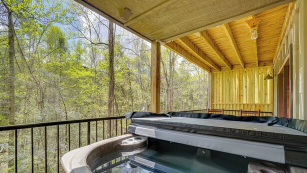 A hot tub with a wooden deck and railing, surrounded by trees. - 3BR Gatlinburg Retreat w/ Hot Tub & Balconies (Gatlinburg)