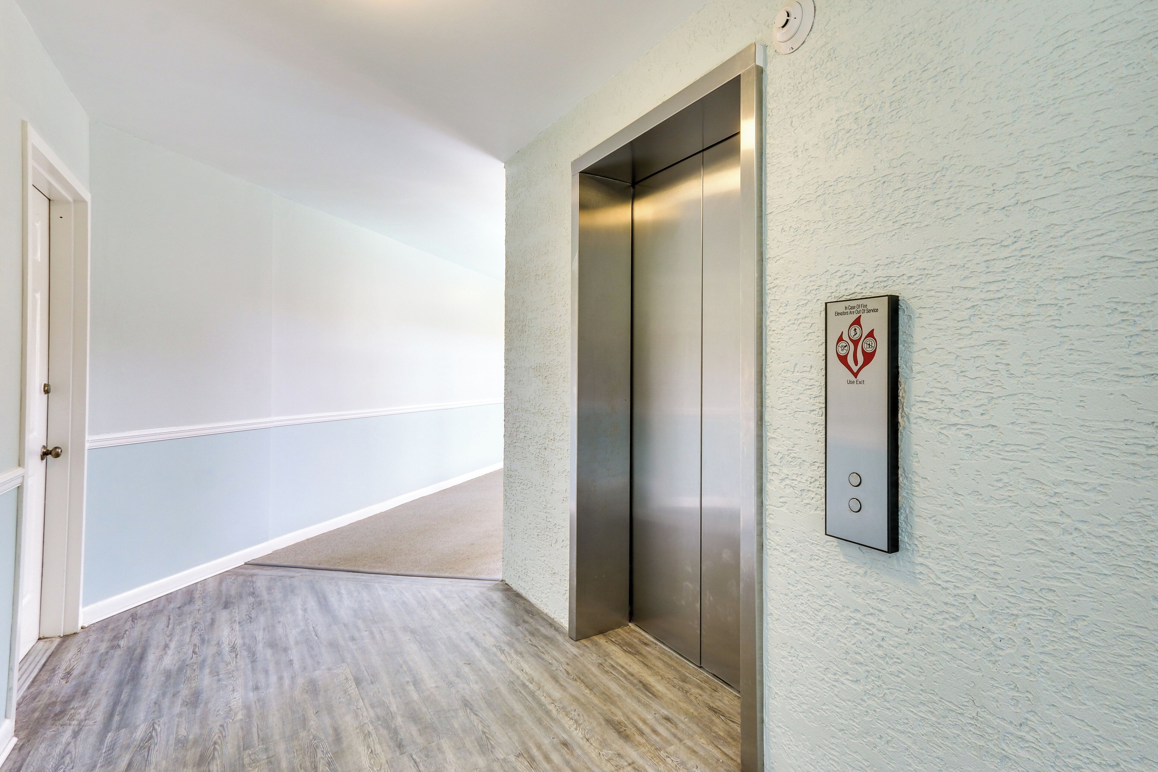 A hallway with a wooden floor, a white door, and a wall-mounted elevator.