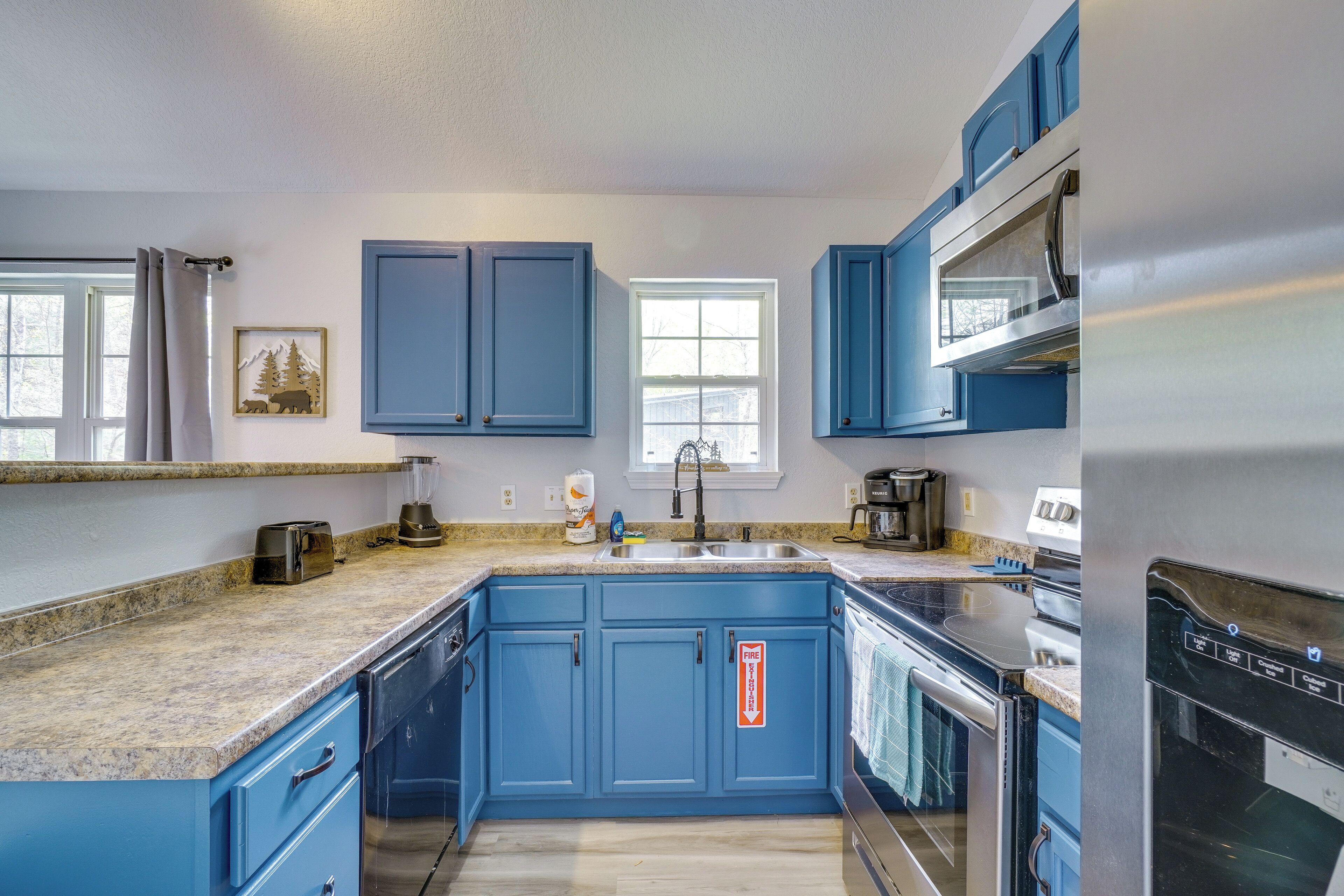 Una cocina con armarios azules, encimera de granito, horno de acero inoxidable y ventana con vista a árboles.