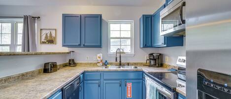 Una cocina con armarios azules, encimera de granito, horno de acero inoxidable y ventana con vista a árboles.