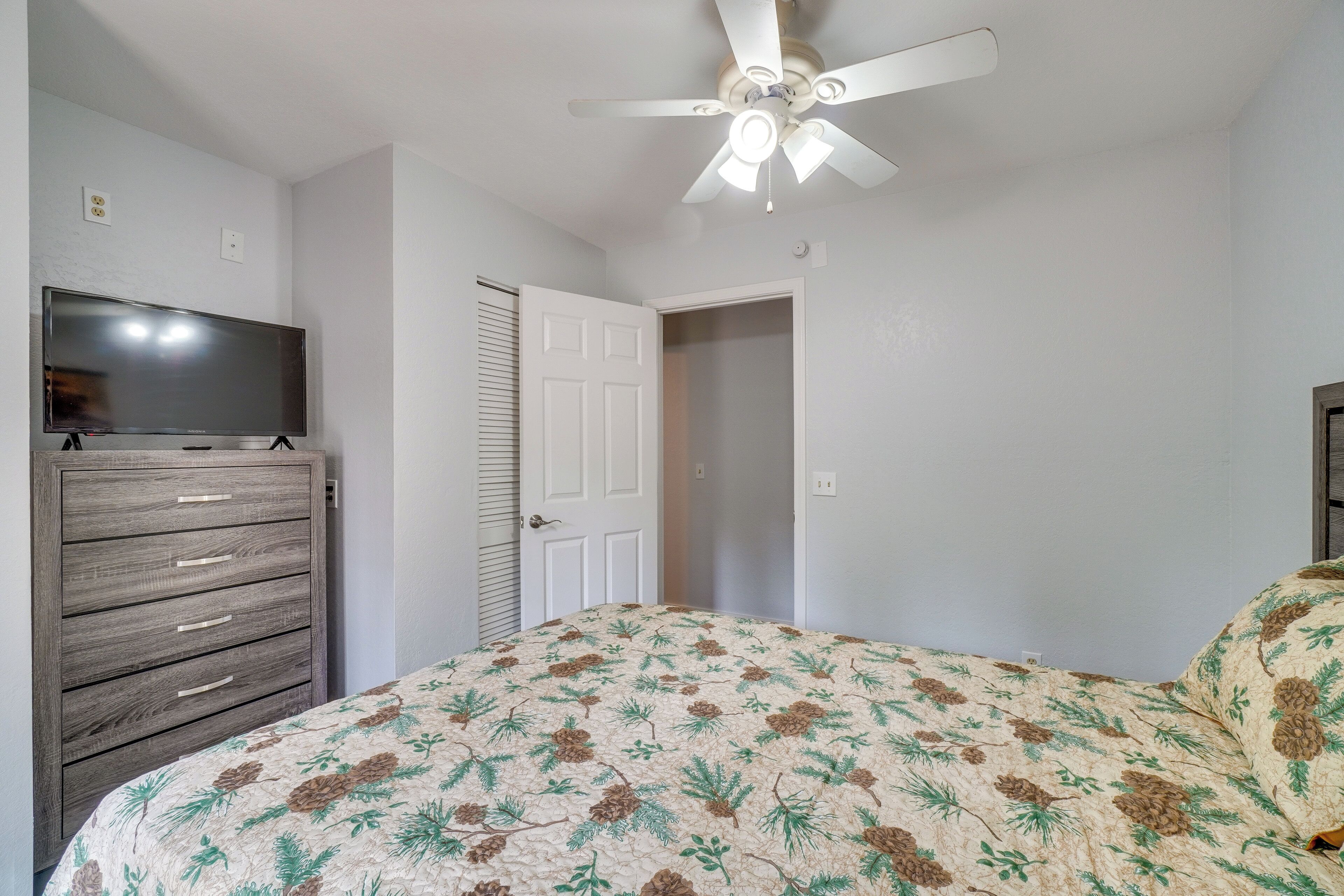 A bedroom with a bed, a dresser, a ceiling fan, and a door.