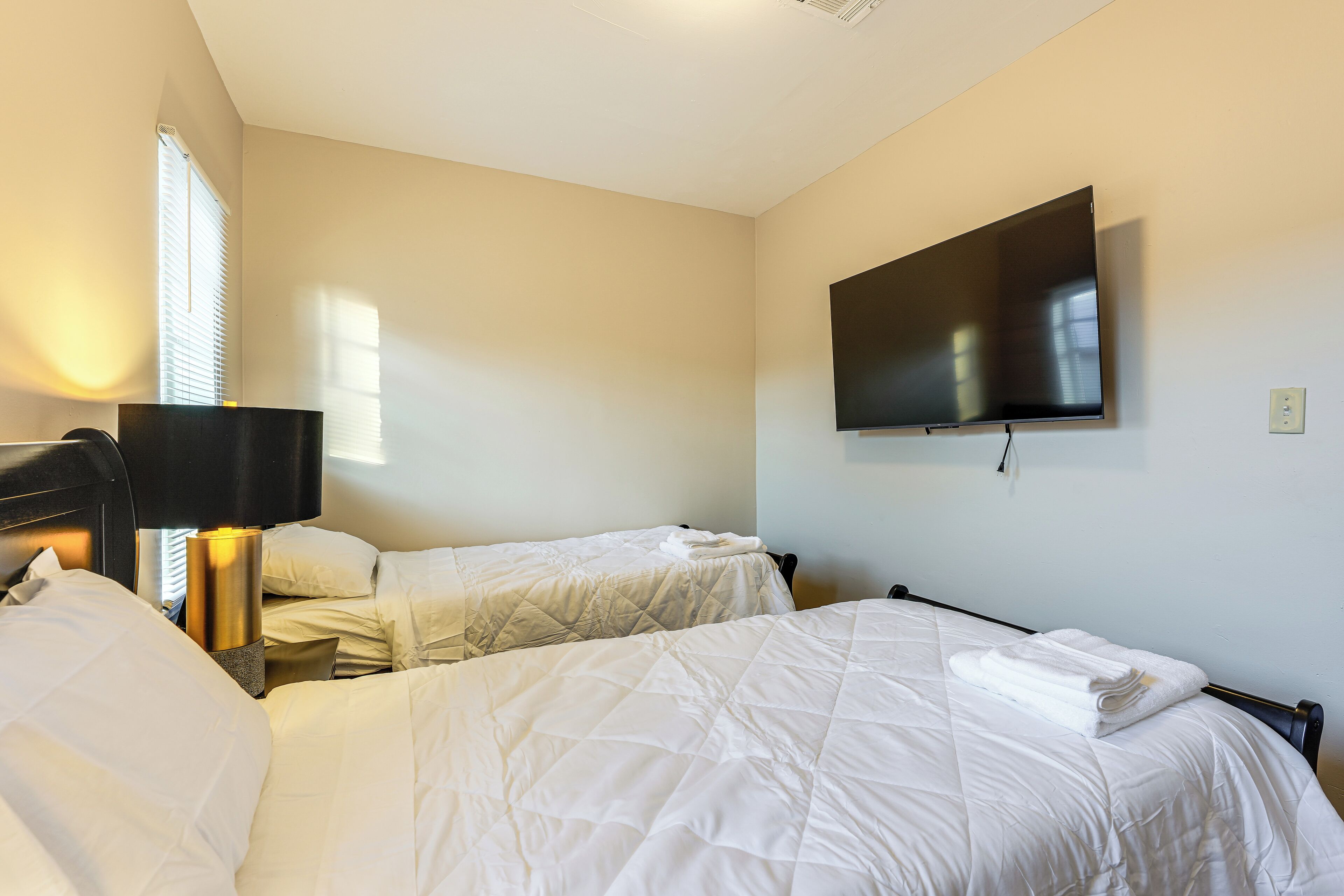 A hotel room with two beds, a flat-screen TV mounted on the wall, and a bedside lamp.