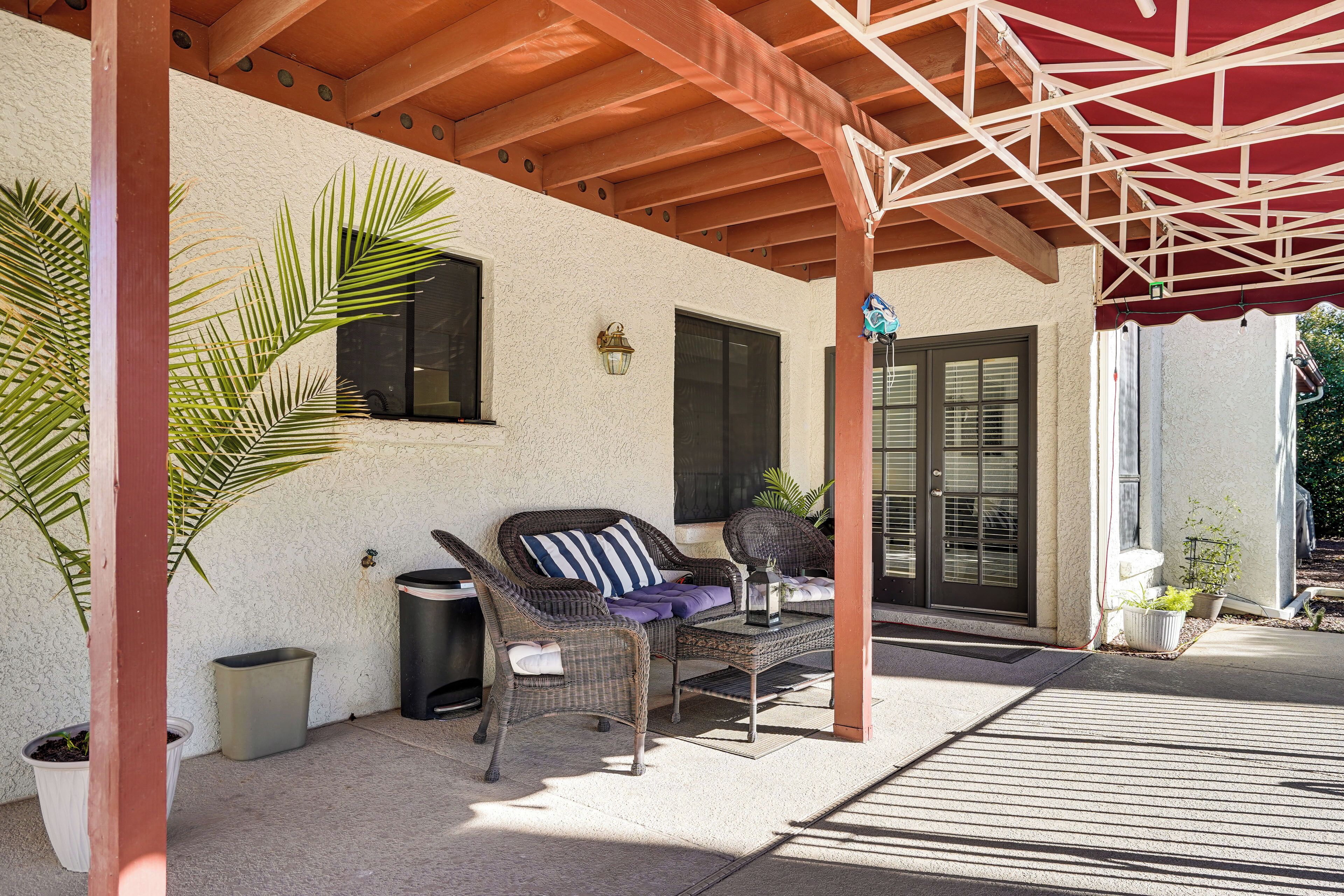 Ein überdachter Patio-Bereich mit Korbmöbeln, Topfpflanzen und einem roten Sonnenschirm.