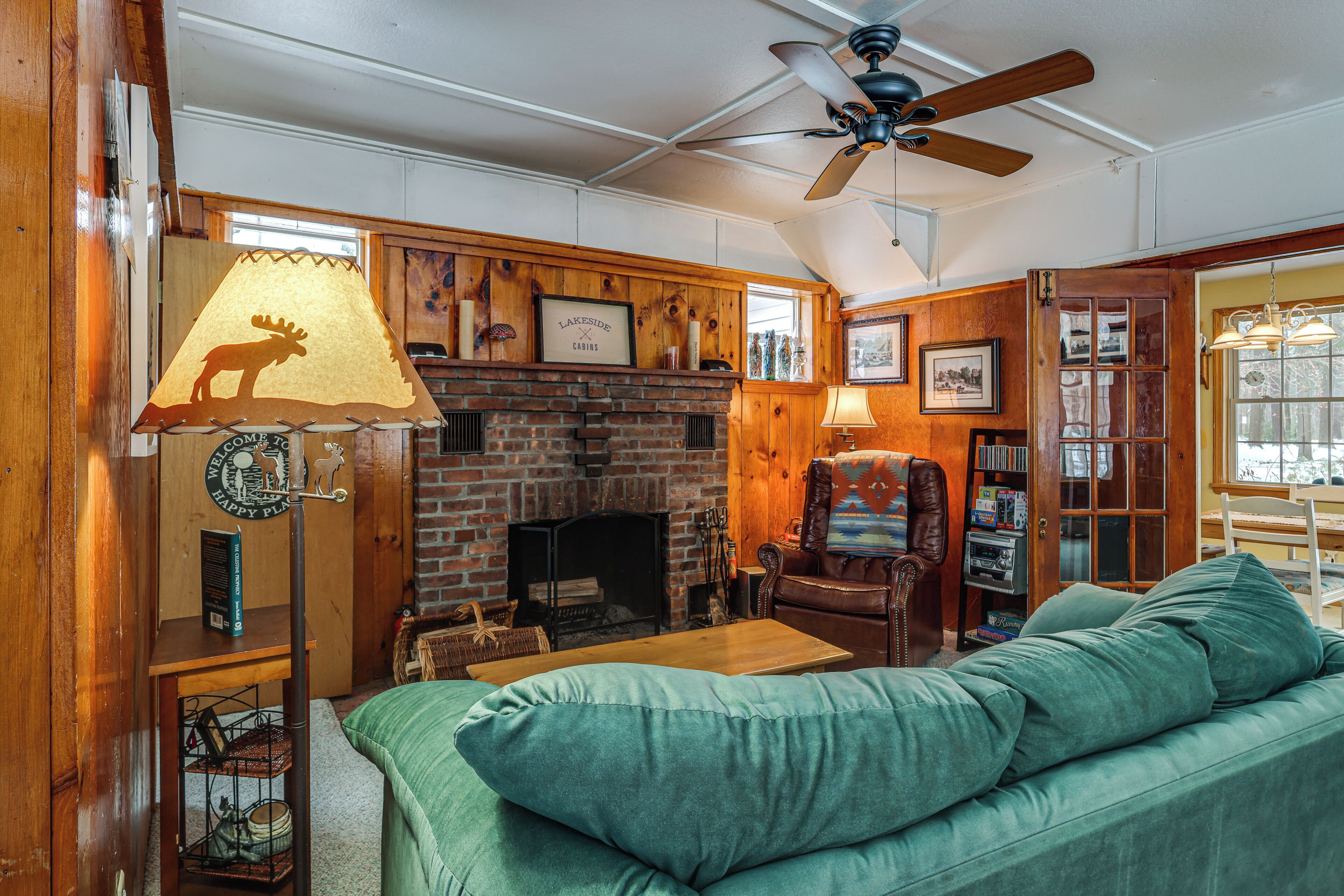 A cozy living room with a fireplace, a green sofa, wooden walls, and a ceiling fan.
