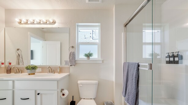 Une salle de bain moderne avec une douche à l’italienne en verre, un lavabo blanc avec un meuble-vasque et une fenêtre située au-dessus des toilettes.