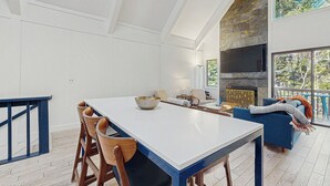 Un vaste espace de vie comprenant une grande table blanche, des chaises en bois, un canapé bleu et une cheminée en pierre.