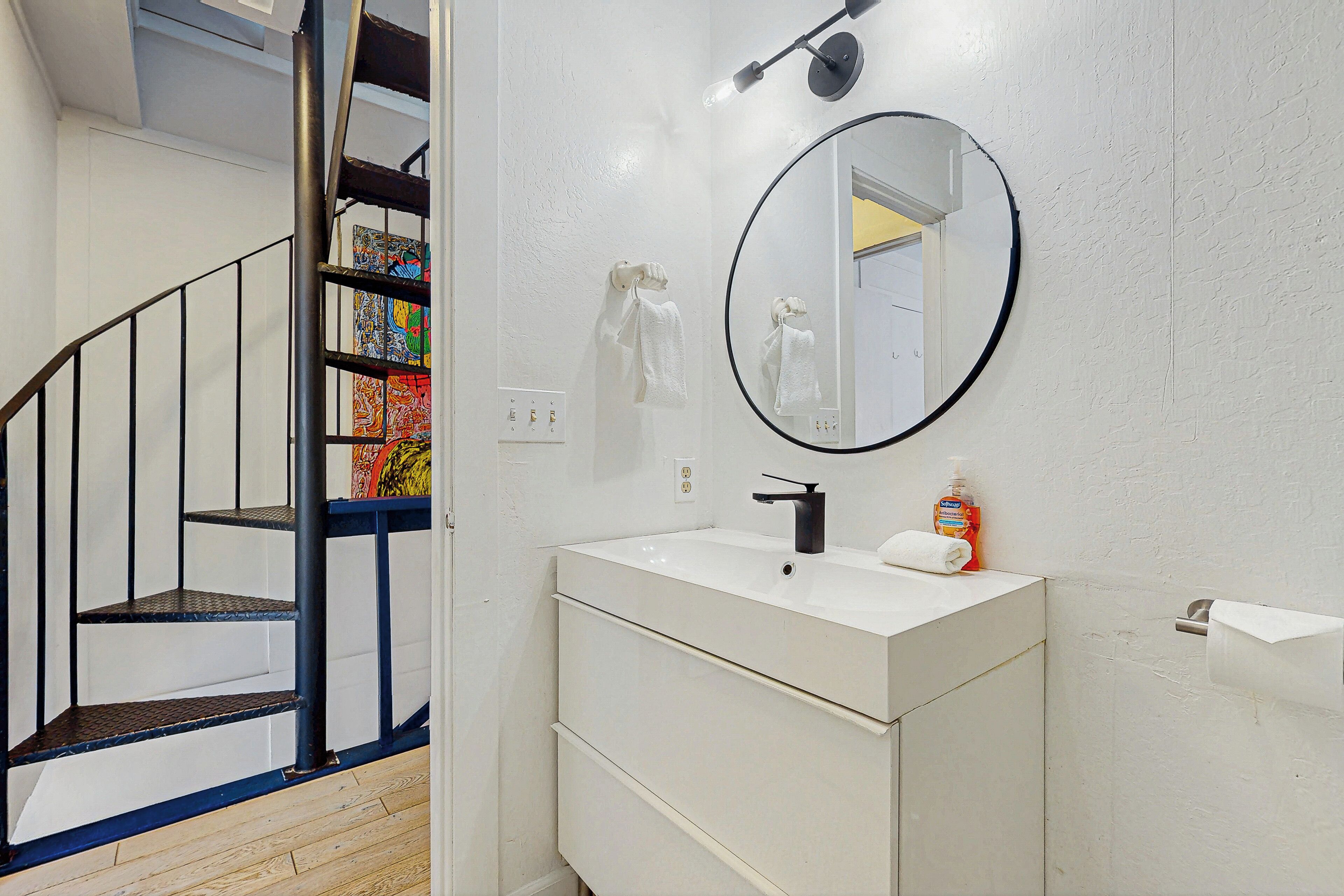 A bathroom with a white vanity, a round mirror, a towel rack, and a shelf with colorful items.