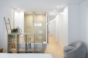 A modern hotel room with a bed, a grey armchair, a wooden shelf with a bicycle, and a large mirror. - Marques DE Pombal Grand Prestige by Homing (Lisbon)