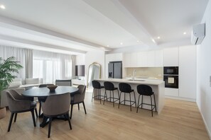 A modern kitchen with white cabinets, a central island with bar stools, and a dining area with a round table and chairs. - Marques DE Pombal Grand Prestige by Homing (Lisbon)