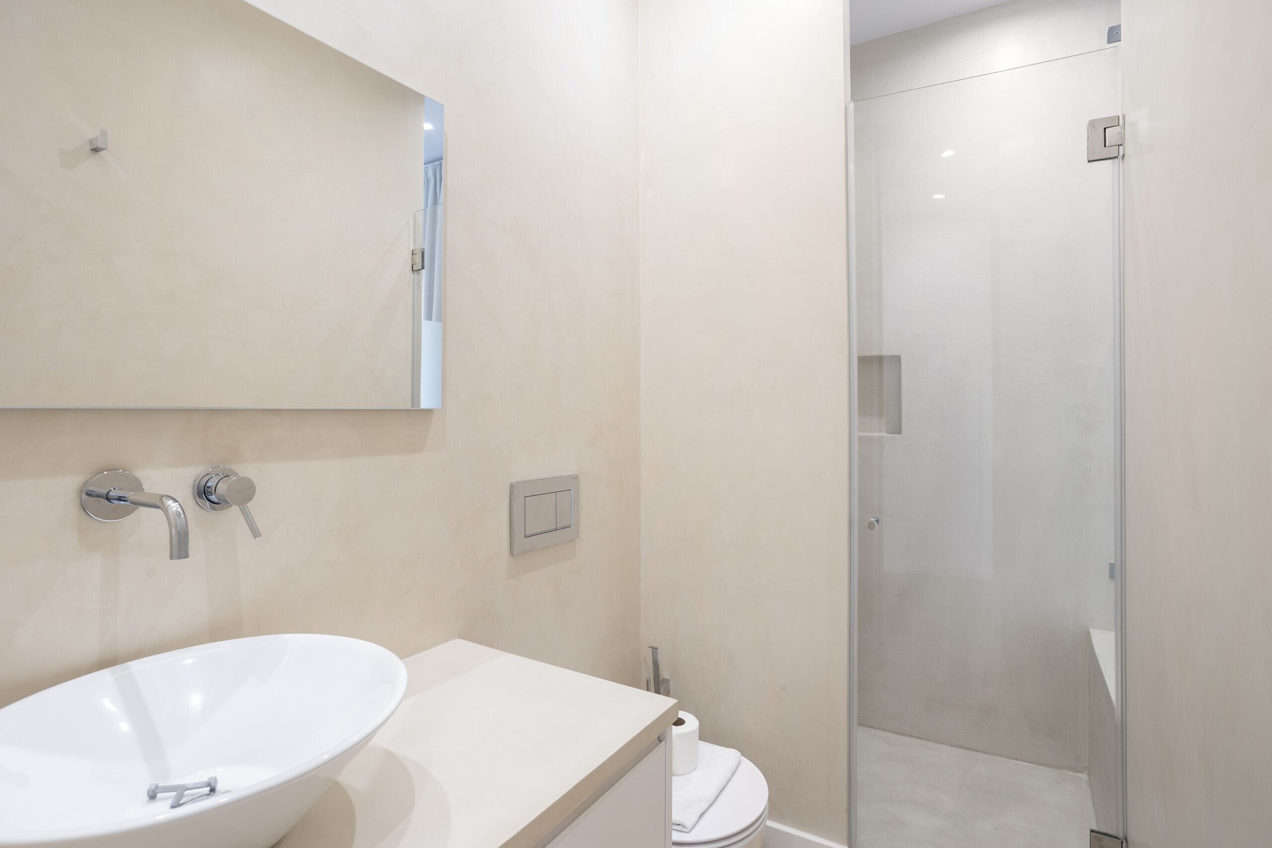 A modern bathroom with a white sink, a mirror, and a glass-enclosed shower.