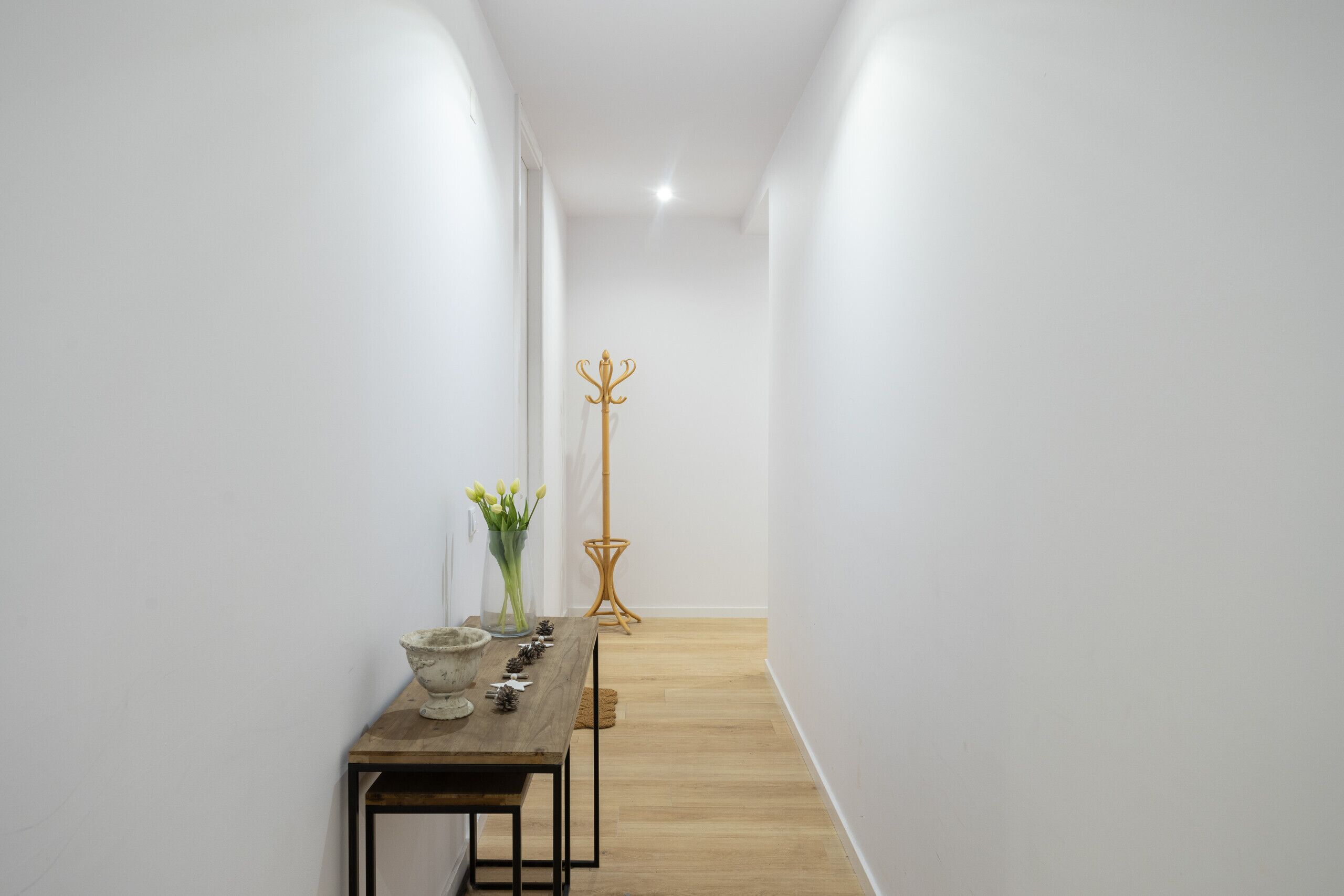 Un pasillo estrecho con una mesa de madera, un florero y un perchero.