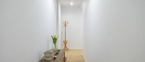 Un pasillo estrecho con una mesa de madera, un florero y un perchero.