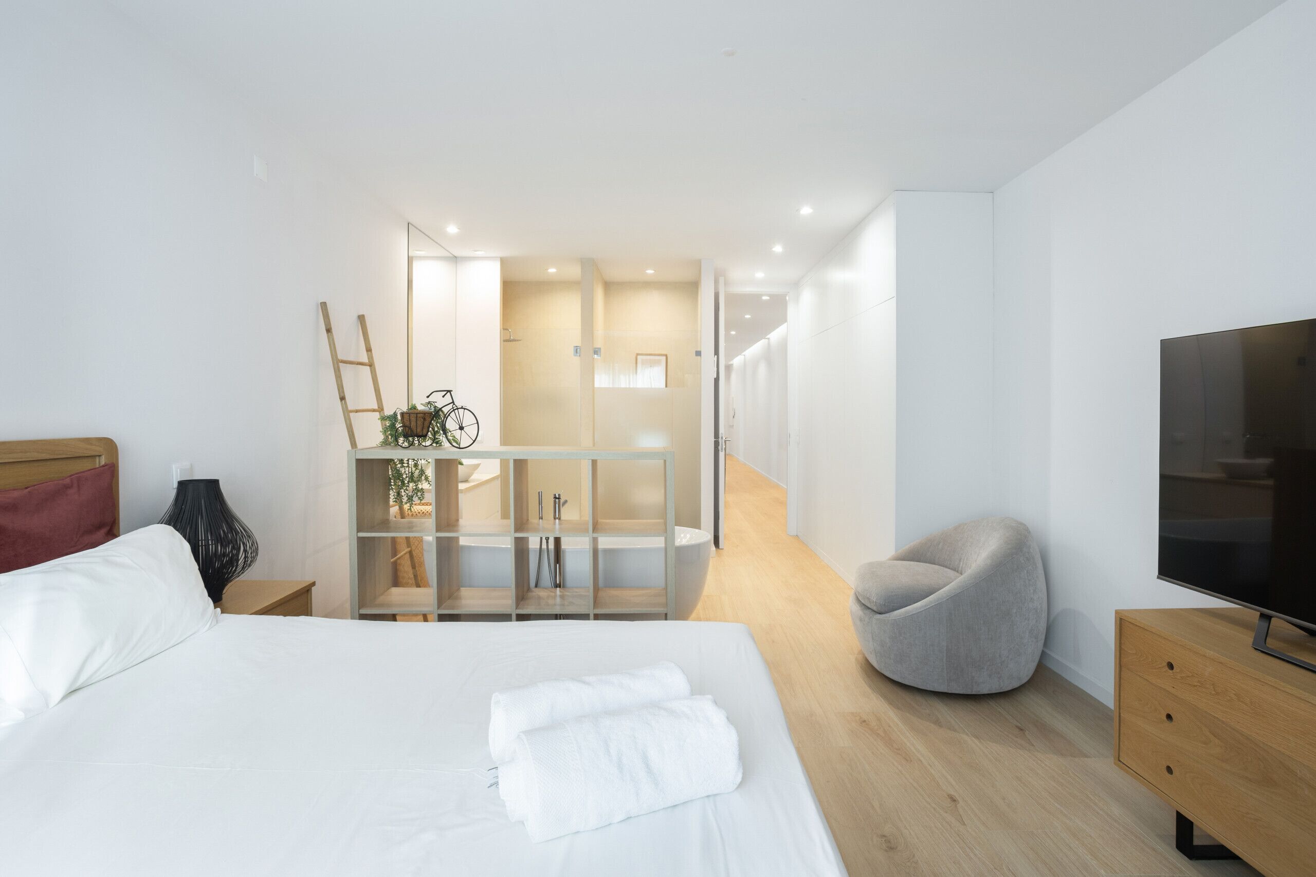 A modern hotel room with a large bed, a TV, a seating area, and a bathroom visible through a glass partition.