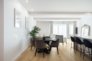 Ein moderner Essbereich mit einem runden Tisch, vier Stühlen, einer Zimmerpflanze und einer Couch im Hintergrund.