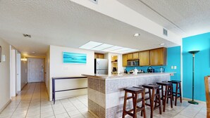 Una cocina moderna con una isla central, taburetes de bar y vista al pasillo.
