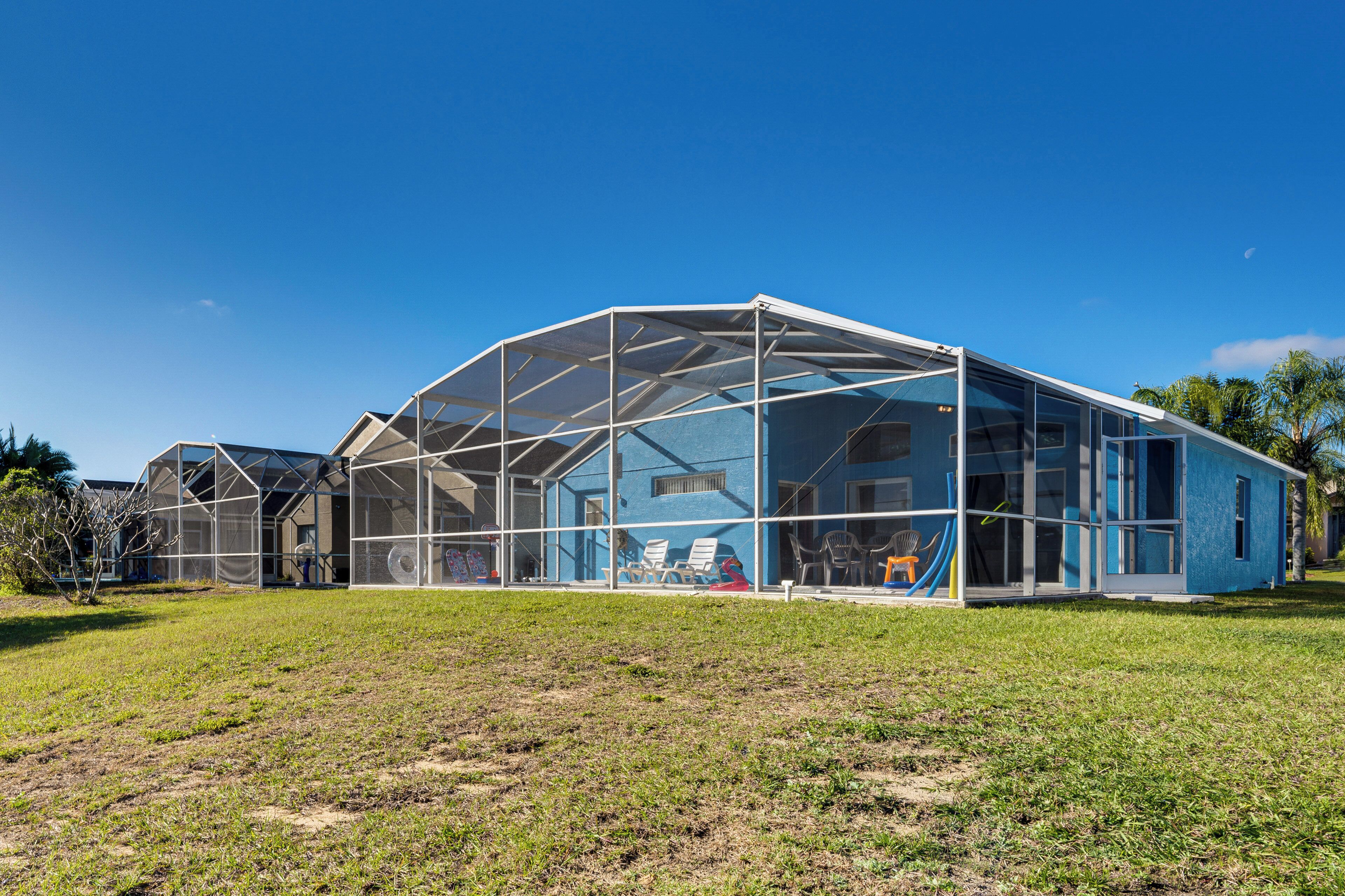 Une structure moderne en verre, au design géométrique, entourée d’une pelouse et de palmiers.