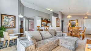 Una sala de estar con sofá modular, mesa de comedor, sillas y una cocina con armarios y microondas.