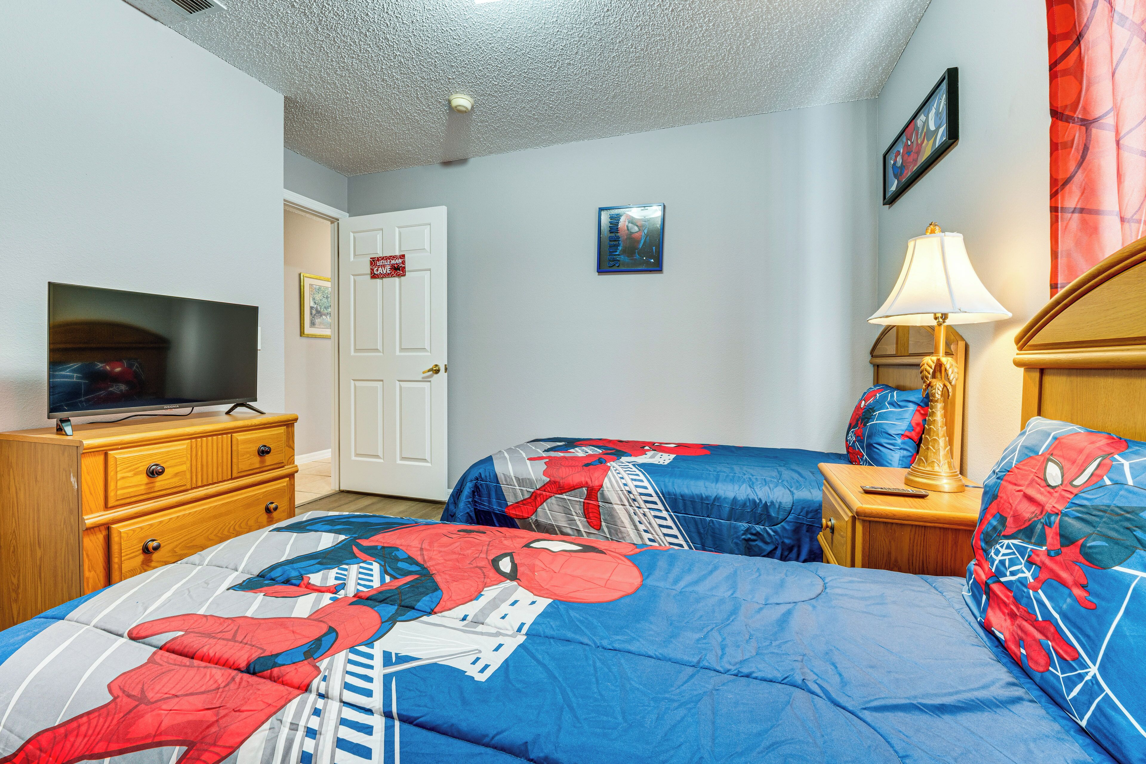 A bedroom with two beds, a TV, a wooden dresser, a lamp, and a door.