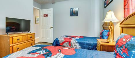 A bedroom with two beds, a TV, a wooden dresser, a lamp, and a door.