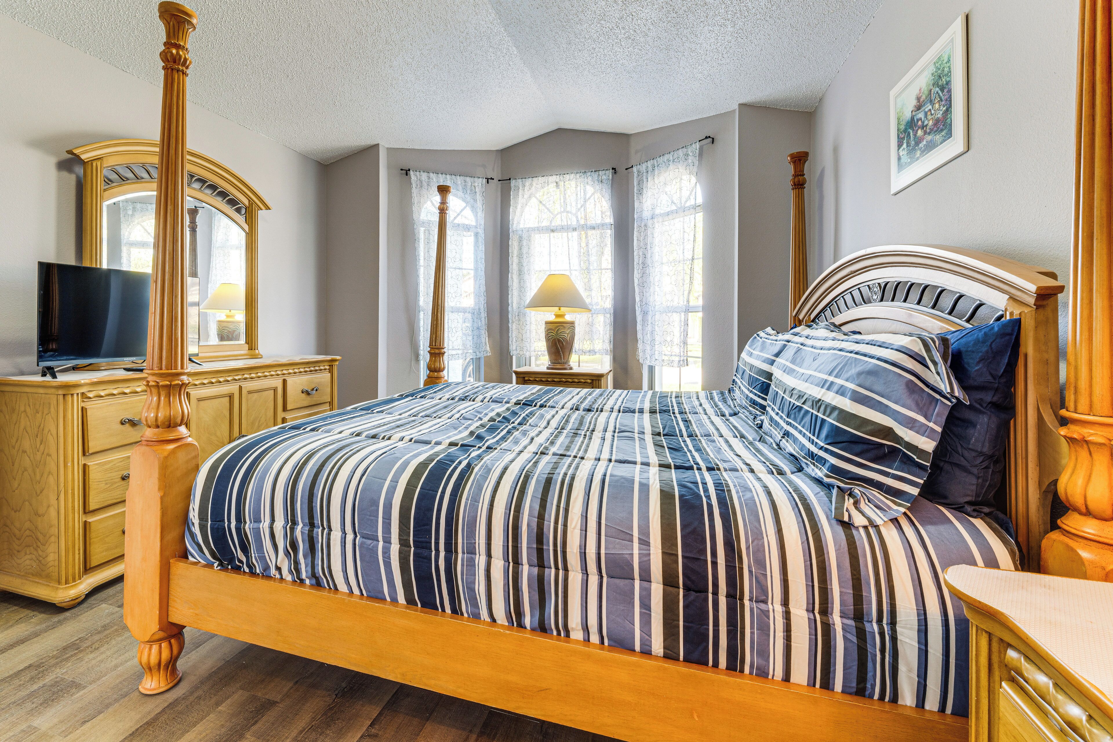 A bedroom with a four-poster bed, a wooden dresser, a television, and a window with curtains.