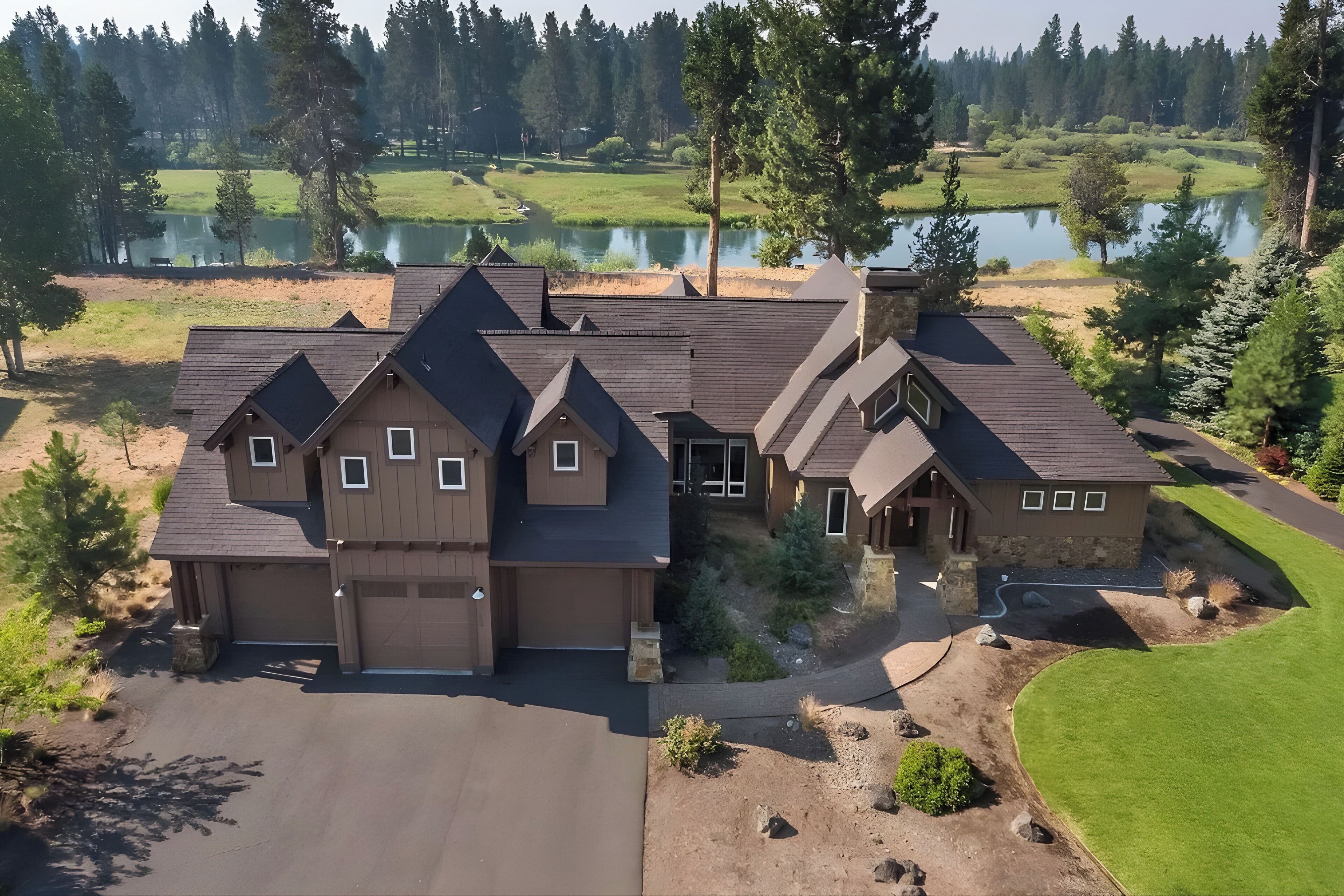 A large, multi-story house with a garage, surrounded by a well-maintained lawn and a lake.